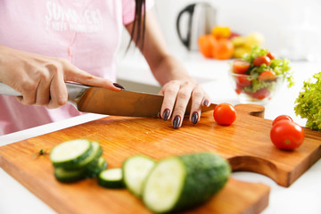 Close-up of woman's hands cutting tomatoes on the wooden board