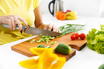 Woman in yellow shirt cuts green onion in the kitchen