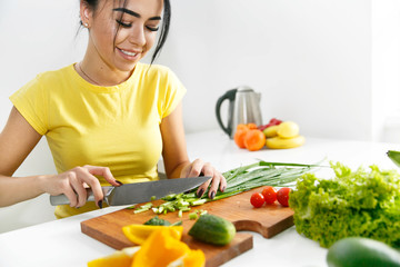 Woman in yellow shirt cuts green onion in the kitchen
