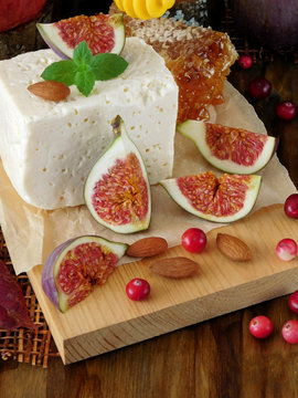 Cheese made of sheep milk and slices of figs on a wooden board surrounded by cranberries and almond. Ingredients for a cheese plate