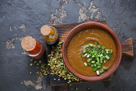 Pea soup with curry served in a clay bowl, top view on a brown stone background, horizontal shot