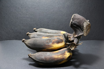 Ripe cultivated banana on the black floor and black background. Thai yellow banana but now ripe to black. Thai name “Kluai Namwa”