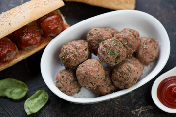 Bowl of baked beef meatballs with homemade sandwiches in the background, studio shot