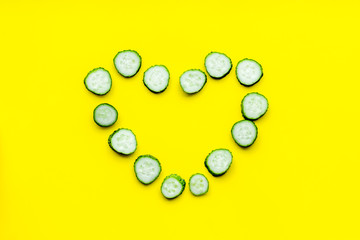 Sliced cucumber in shape of heart on yellow background top view copyspace