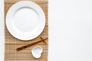 Table setting for sushi roll. Empty plate on mat near chopstick and bowl for sause on white background top view copyspace