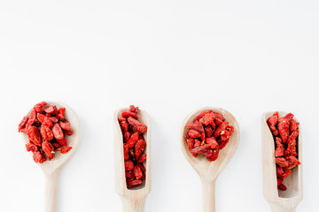 Wooden spoons with dried goji berries on white background top view copyspace