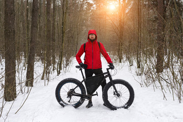 The man in red jacket stands near the fatbike in the winter