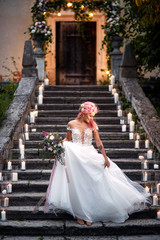 Fototapeta na wymiar Bride with pink hair and tattoos on her tender shoulder stands on footsteps with shiny candles