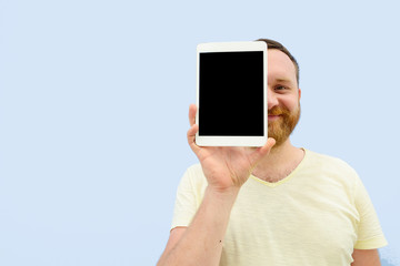 cheerful man with a red beard hiding behind shows a tablet close-up, space for text