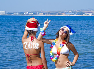 Two girlfriends in a Santa hat during a beach holiday. Girl with the inscription 2018 on the back. ...