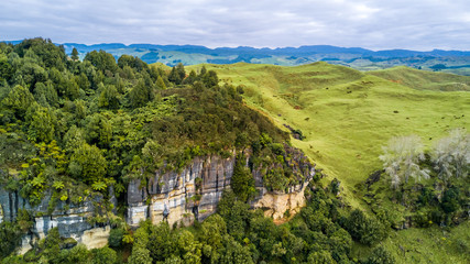 Fototapeta na wymiar Aerial view on a rocky cliff with forest and farmland on the background. Taranaki region, New Zealand