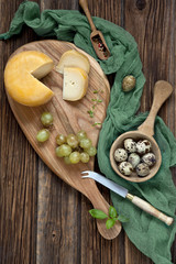 Cheese, grapes and quail eggs on rustic wooden background. Top view, background