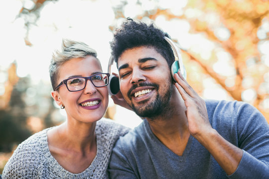 Young mixed race couple listening to music on headphones outdoors