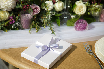White present box with violet ribbon stands on a dinner table