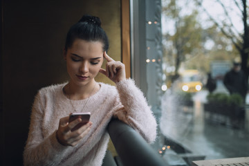 Adult girl using smartphone in cafe sit at window