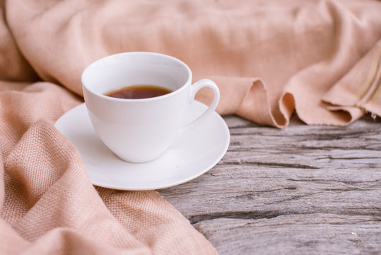 White cup of coffee on the wooden table with scarf