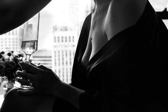 Woman in black silk robe with opne shoulders and breast holds glass with champagne