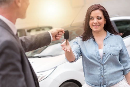 Car salesman handing car keys to young woman, light effect