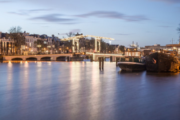 Obraz premium Old historic dutch bridge, Amstel river, and boats in the evening at the twilight blue hour, Netherlands