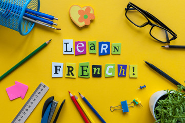 Word LEARN FRENCH made with carved letters on yellow desk with office or school supplies,...