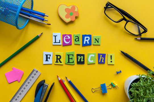 Word LEARN FRENCH made with carved letters on yellow desk with office or school supplies, stationery. Concept of Franch language courses