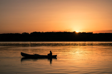 Fisherman with a both in the river on sunset