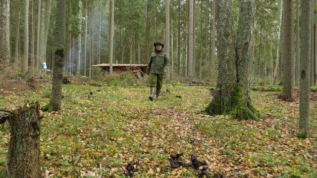 Hunter in camouflage walks in autumn forest near hunting hut, steadicam shot