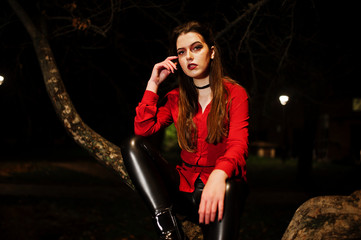 Black girl in red shirt and bright make-up on night street sitting on scary tree outdoor. Halloween theme.