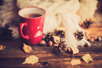 Mug of hot coffee in a woman's hand in a sweater in the autumn setting on a wooden table with a knitted scarf, sweater. Comfort, warmth, cozy