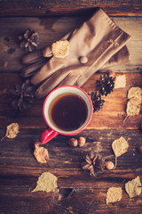 Hands in red knitted gloves holding a hot cup of coffee against yellow leaves background. Concept of autumn time, warmth and coziness