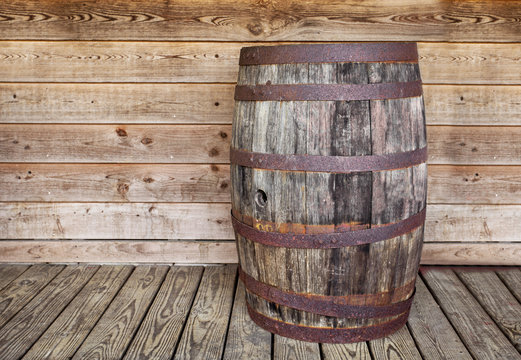 A vintage empty alcahol wooden keg sitting on a wood plank floor against a wood board wall