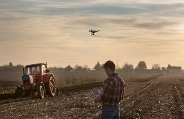 Farmer navigating drone above farmland - obrazy, fototapety, plakaty