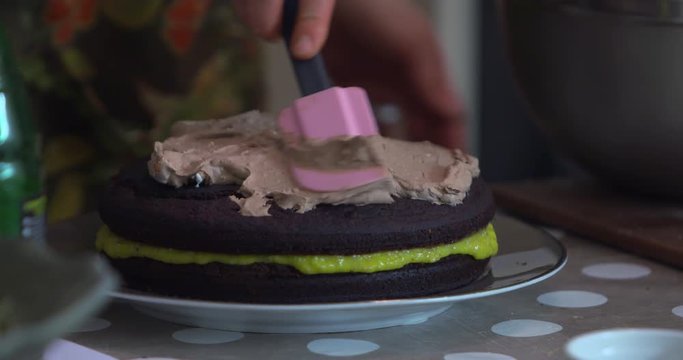 Chef spoons chocolate icing onto layered mango and chocolate sandwich cake with palette knife II