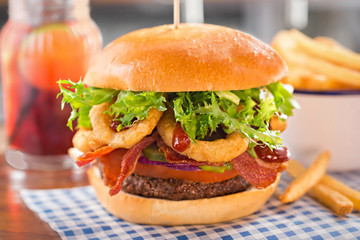Burger with beef, tomato, onion, pickles, bacon, onion rings, lettuce and barbecue sauce.