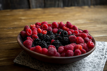 fresh raspberries and blackberries in a ceramic bowl on a wooden table