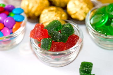 A close-up of red and green sugar-coated jelly candies in a glass bowl. The chewy gummy candies...