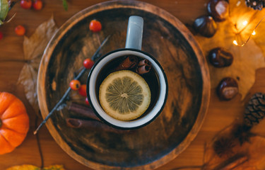 Glass of hot steaming tea and autumn plants on wooden table .