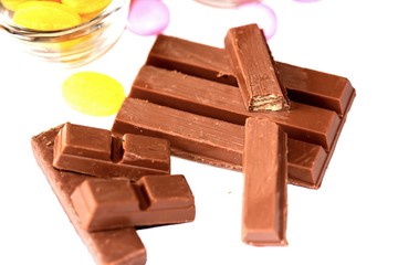 A close-up of milk chocolate bars broken into pieces, revealing a crispy wafer inside. The rich chocolate is accompanied by colorful candies, creating a tempting and indulgent dessert display