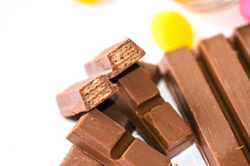 A close-up of milk chocolate bars broken into pieces, revealing a crispy wafer inside. The rich chocolate is accompanied by colorful candies, creating a tempting and indulgent dessert display