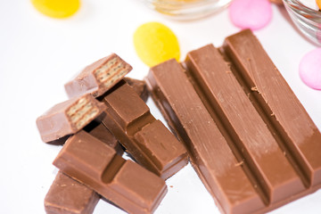A close-up of milk chocolate bars broken into pieces, revealing a crispy wafer inside. The rich chocolate is accompanied by colorful candies, creating a tempting and indulgent dessert display