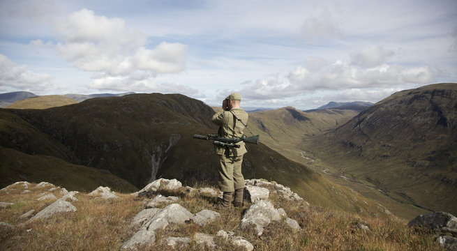 A stalker looks out over the hills with his binoculars