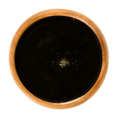 Apple juice concentrate in wooden bowl. Dark brown fruit juice. Syrup made of pressed apples and further treated by dehydration. Sugar substitute and sweetener. Macro food photo from above over white.