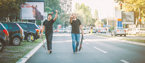 Two pro skateboard rider walking down the street holding their skateboards in hand. Urban skate scene