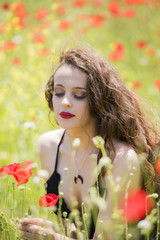 Naklejka premium Pretty young lady wear black long dress with deep neckline sitting amongst poppies in a field