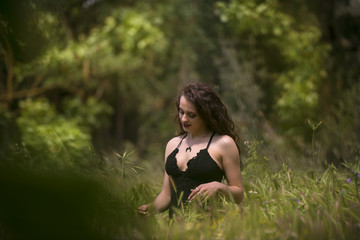 Naklejka na ściany i meble Pretty young lady wear black long dress with deep neckline stands amongst large weeds field
