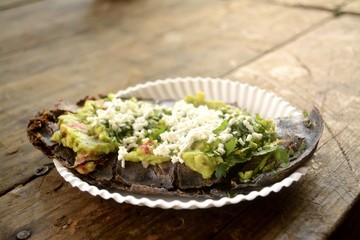 Mexican tlacoyos, a dish made with blue corn and filled with fried beans or broad beans, similar to mexican gordita, with guacamole, spicy sauce, coriander and cheese at the top