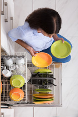 Young Woman Arranging Plates In Dishwasher