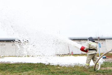 Obraz premium Firefighters extinguish the fire with a chemical foam coming from the fire engine through a hose
