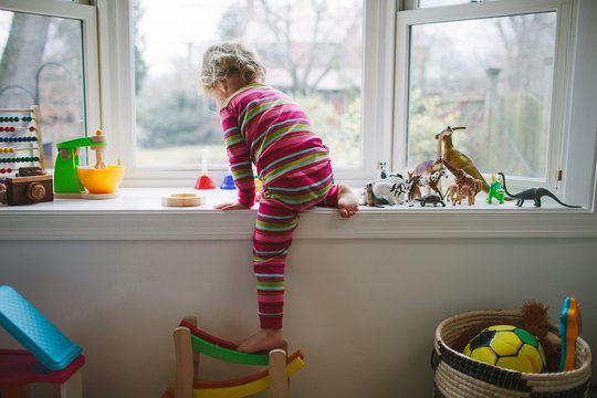 little girl in pajamas playing with toys on a window sill