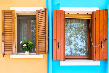 Picturesque windows with shutters on blue and brown walls of houses on the famous island Burano, Venice, Italy